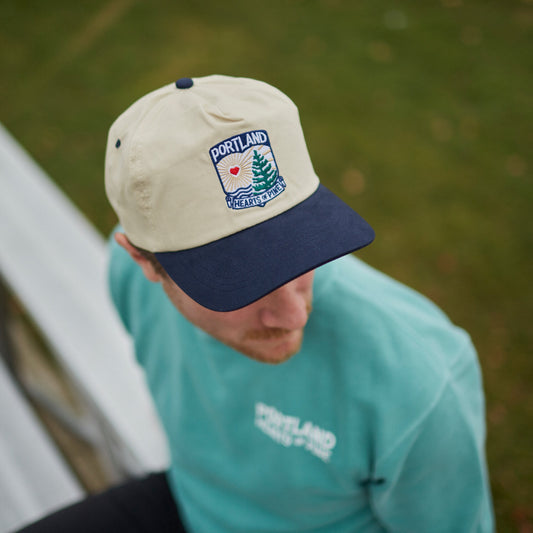 A person wearing a beige cap with 'PORTLAND' and a crest logo on the front and a navy brim.