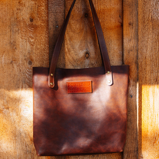 Brown leather tote bag with a visible brand logo on a wooden surface