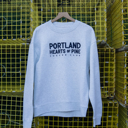 Light blue sweatshirt with 'Portland Hearts of Pine Soccer Club' text on a yellow metal crate background