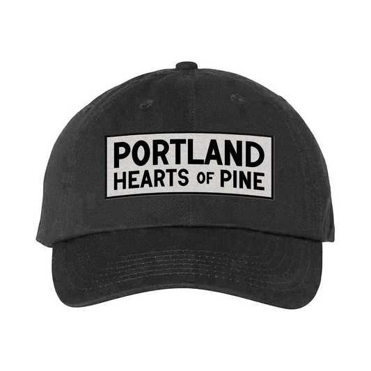 A black cotton dad hat with the text 'PORTLAND Hearts of Pine' embroidered on the front.
