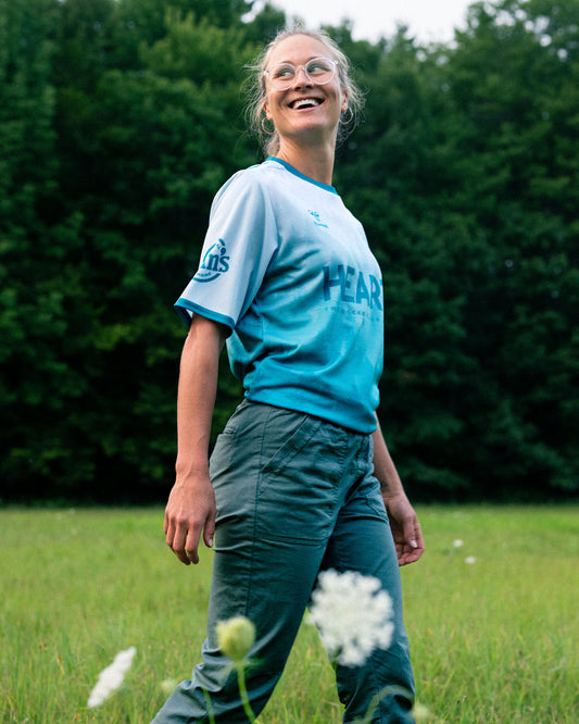 Person wearing a blue t-shirt with text, standing in a grassy field with trees in the background