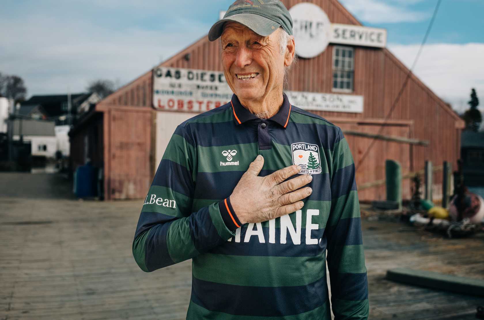 Man wearing a striped shirt with visible branding in front of a red building.